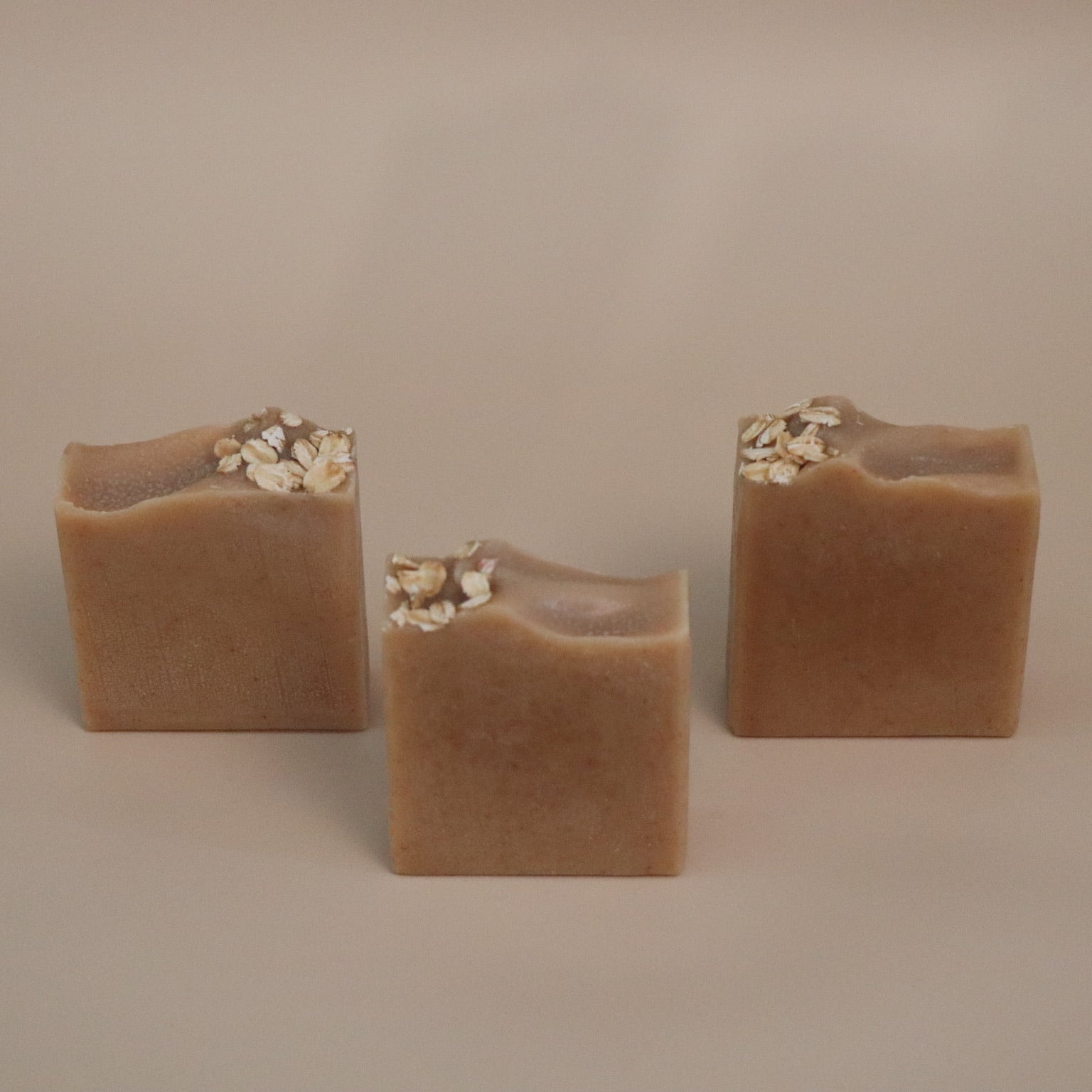 Three square-shaped brown soap bars with oats on a beige background 