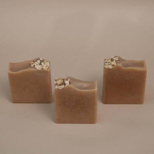 Three square-shaped brown soap bars with oats on a beige background 