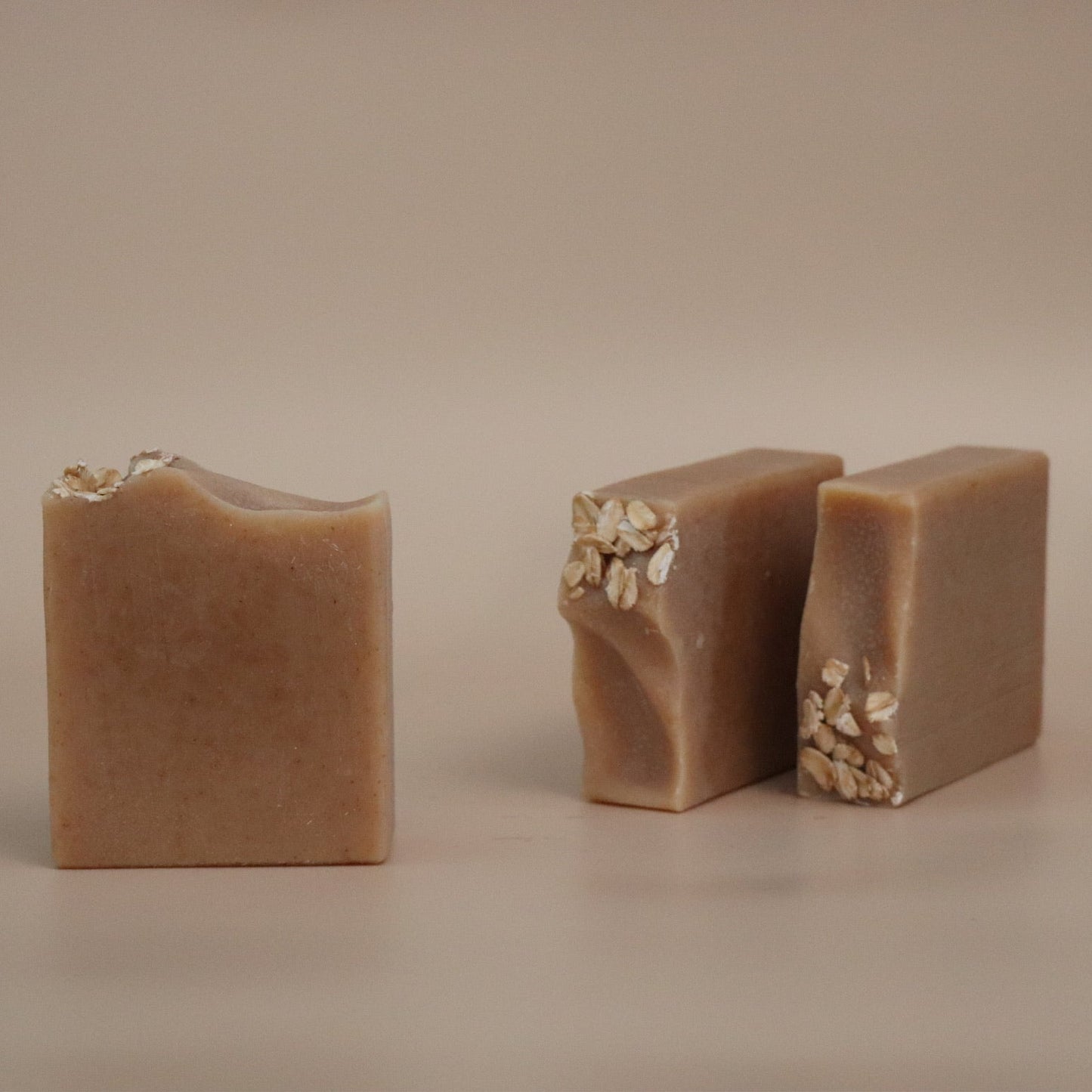 Three pieces of brown soap with visible ingredients on a beige background