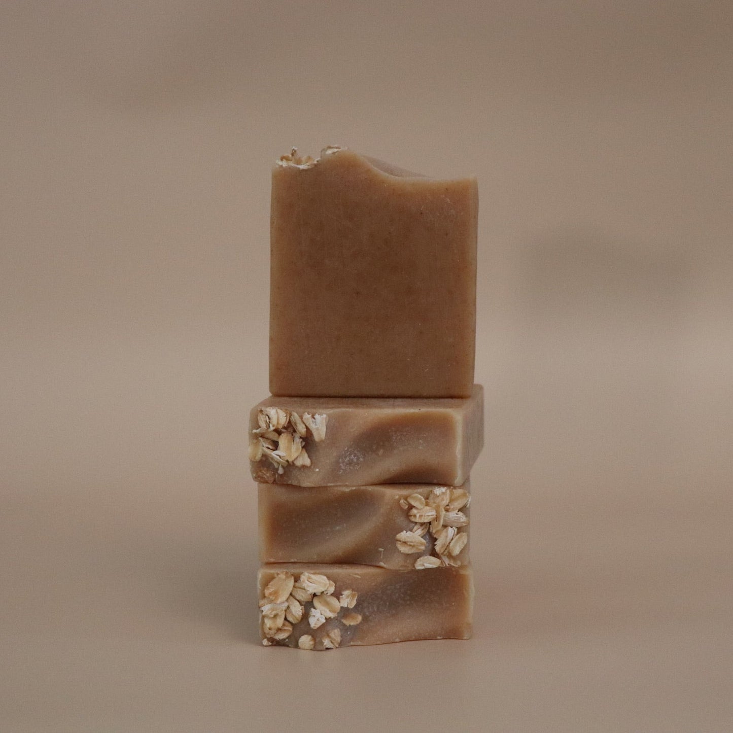 four brown soap bars with visible textures and ingredients on a beige background