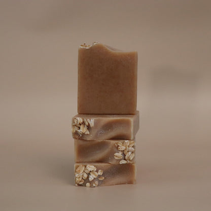 four brown soap bars with visible textures and ingredients on a beige background