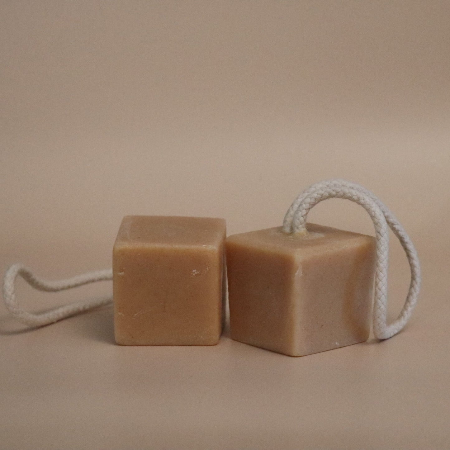Two square bars of soap on a rope against a beige background