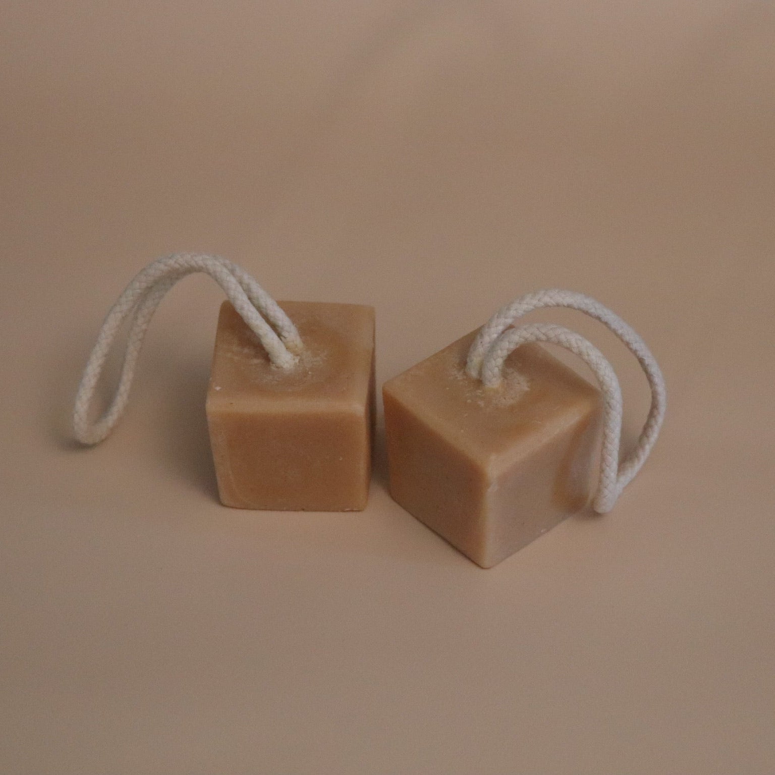 Two brown square soap bars with white ropes on a beige background