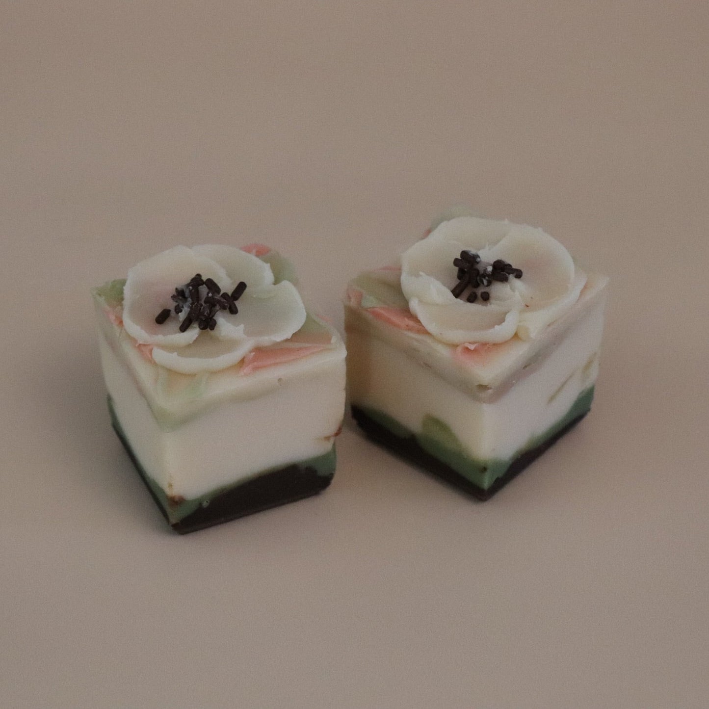 Two small cube soaps with floral toppings on a beige background