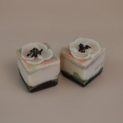 Two small cube soaps with floral toppings on a beige background
