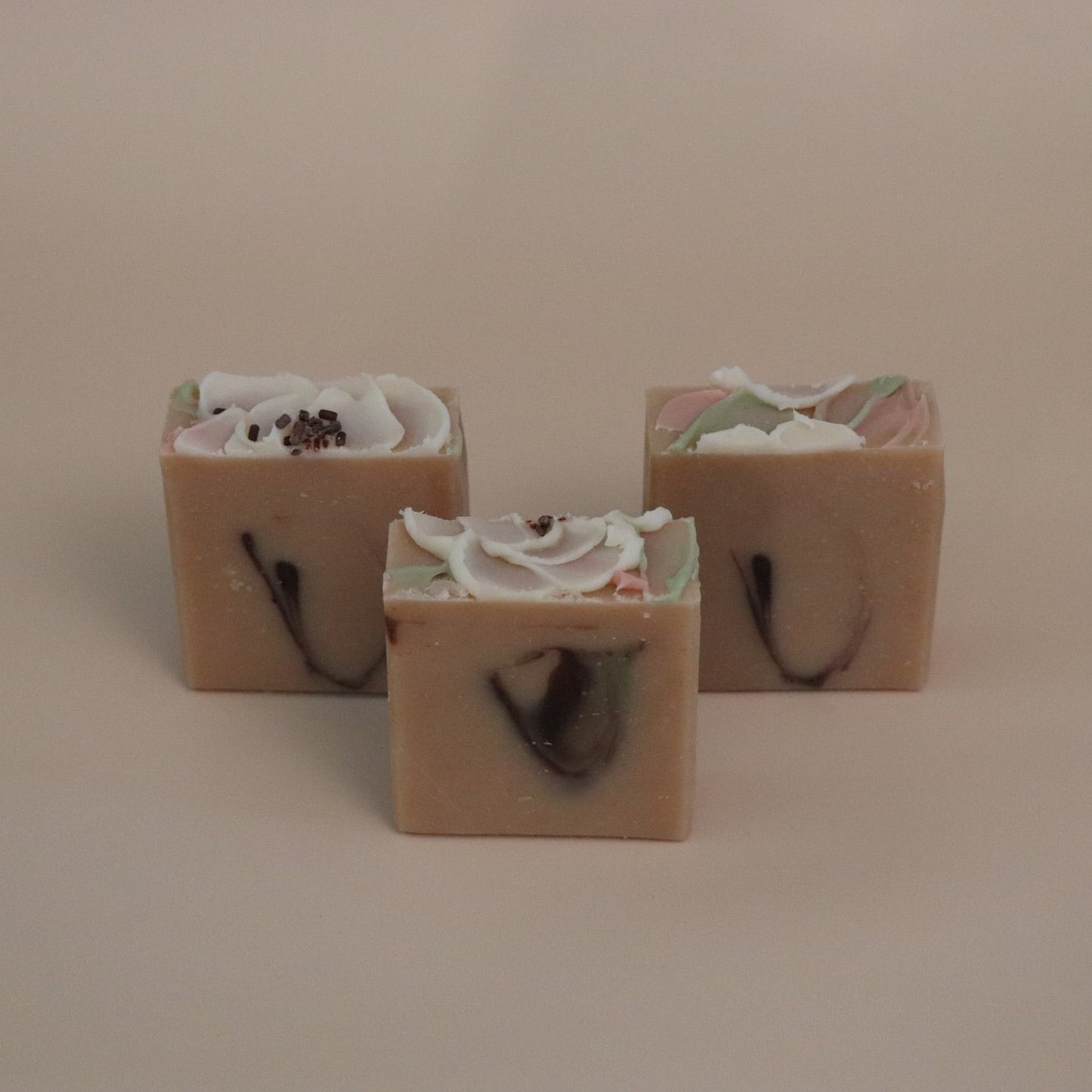 Three square soap bars with floral designs on a beige background
