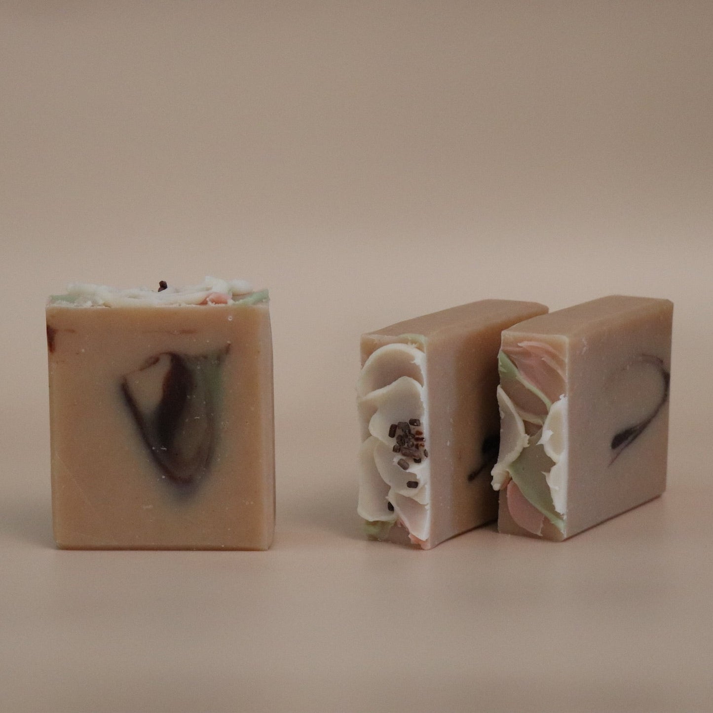 Three bars of soap with visible ingredients on a beige background