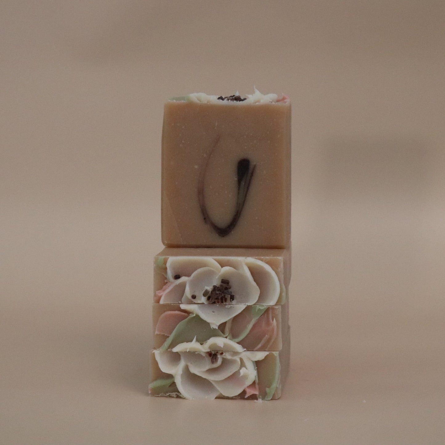 Two stacked soap bars, one plain and one with floral design, on a beige background