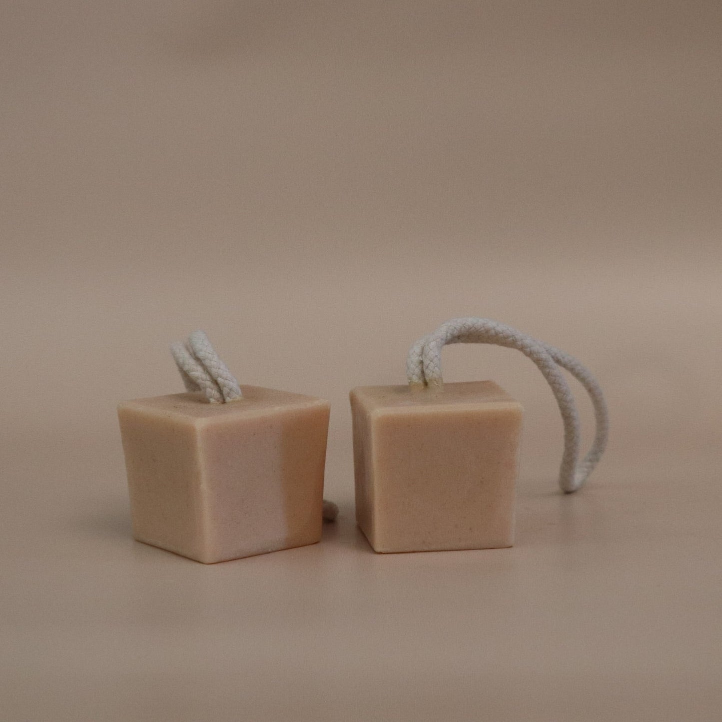 Two cube-shaped soap bars with rope handles on a beige background