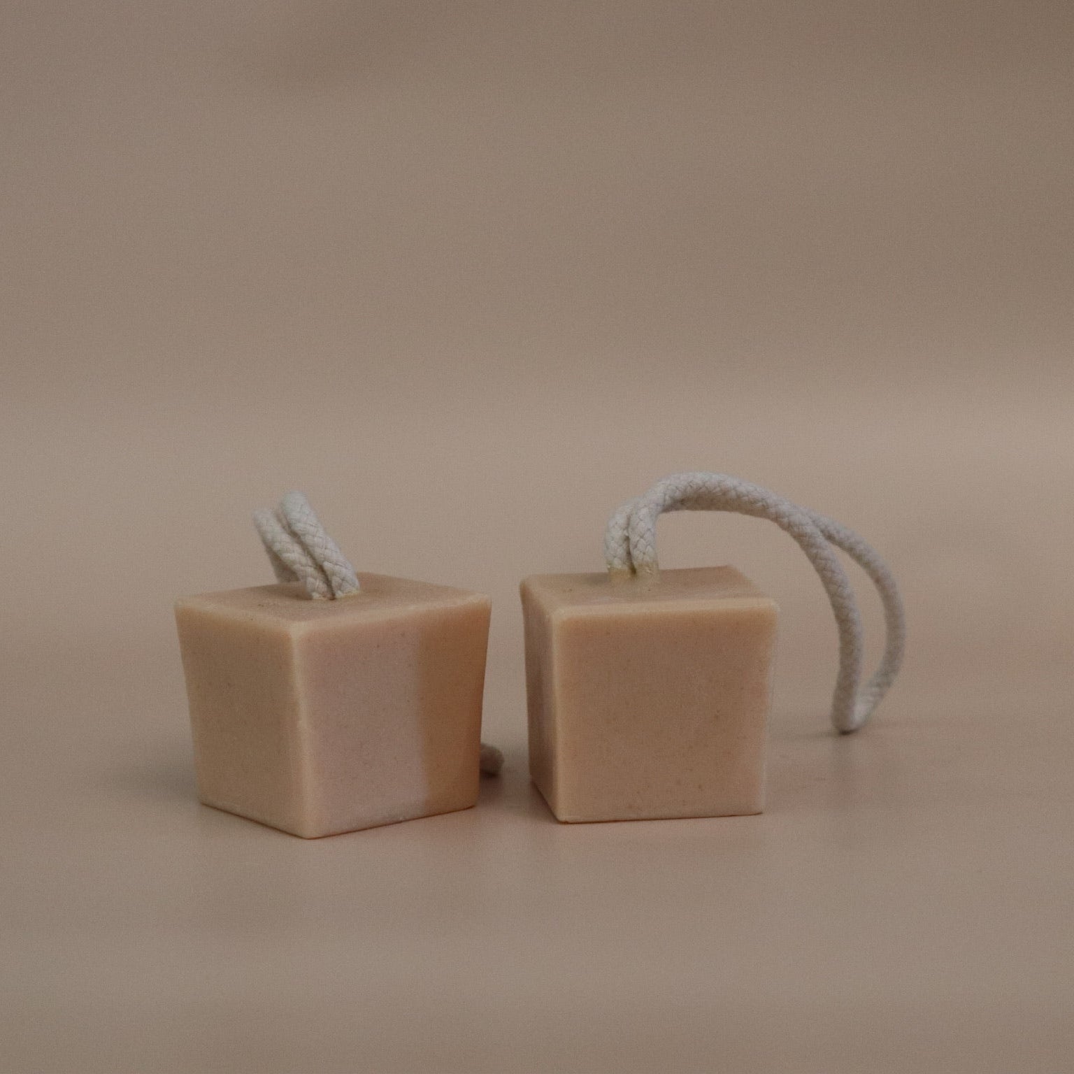 Two cube-shaped soap bars with rope handles on a beige background