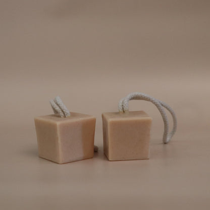 Two cube-shaped soap bars with rope handles on a beige background