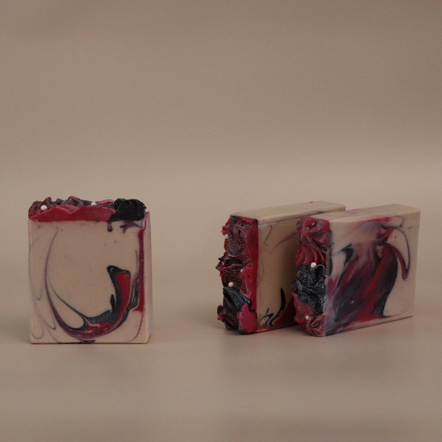 Three marbled soap bars with dark hot pink, beige, and black swirls on a beige background