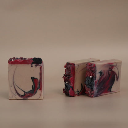 Three marbled soap bars with dark hot pink, beige, and black swirls on a beige background