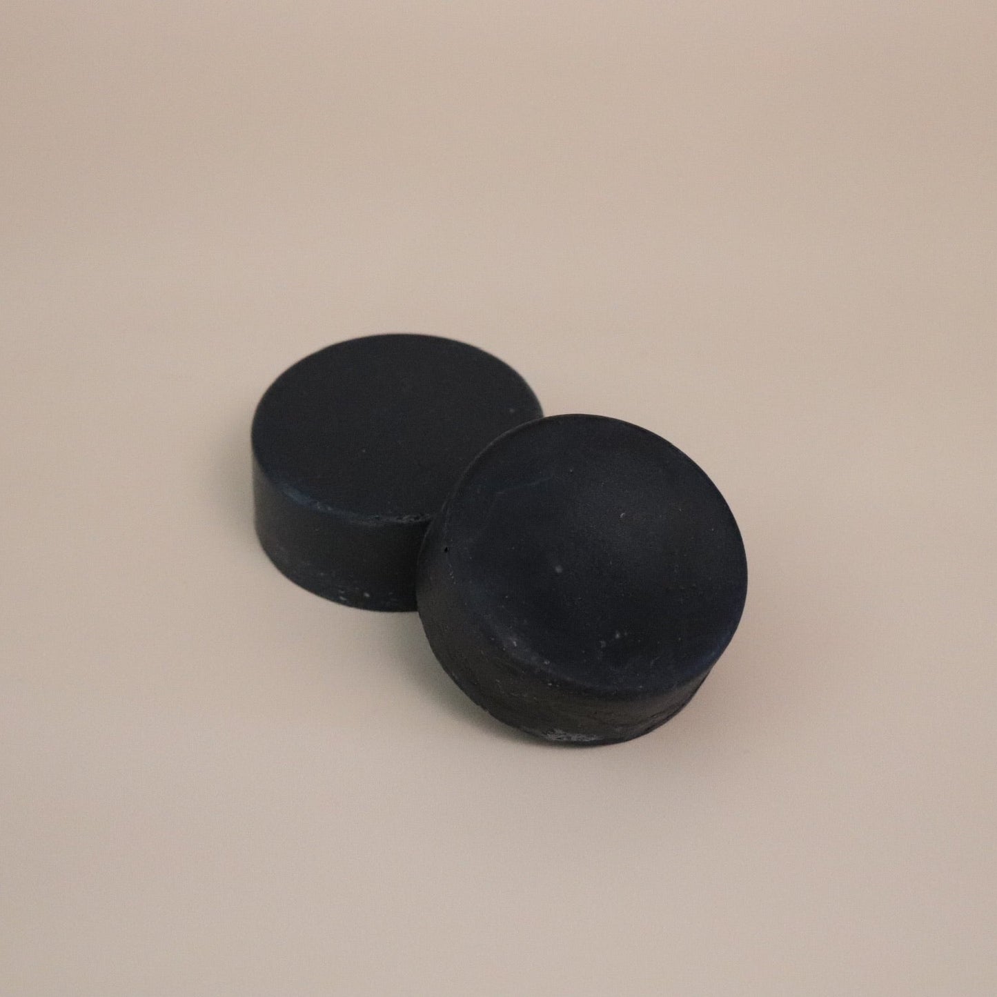 Two black round soap bars on a beige background