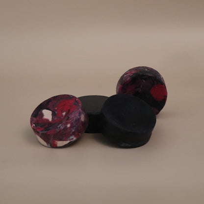 Three marbled black and dark hot pink soap on a beige background