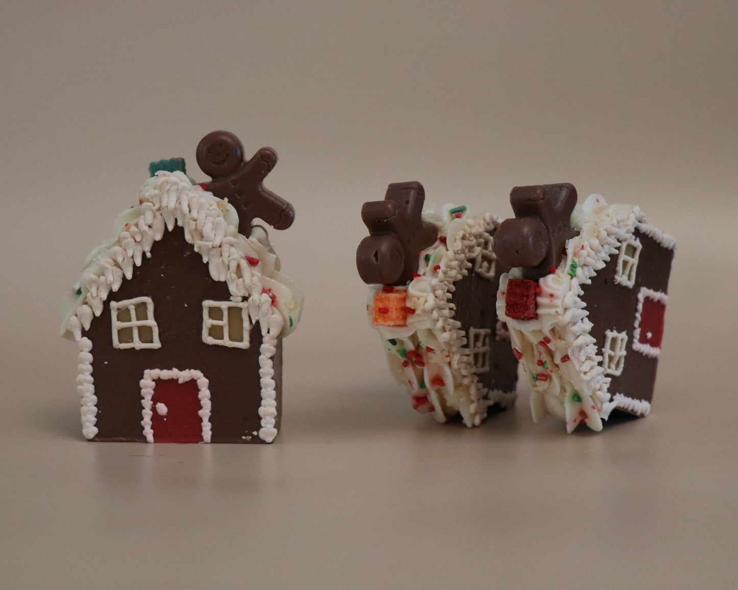 Two gingerbread house-shaped artisan soaps with decorative elements on a plain background