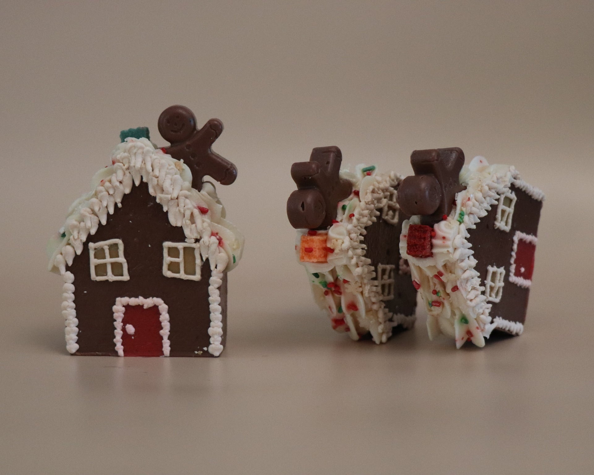Two gingerbread house-shaped artisan soaps with decorative elements on a plain background