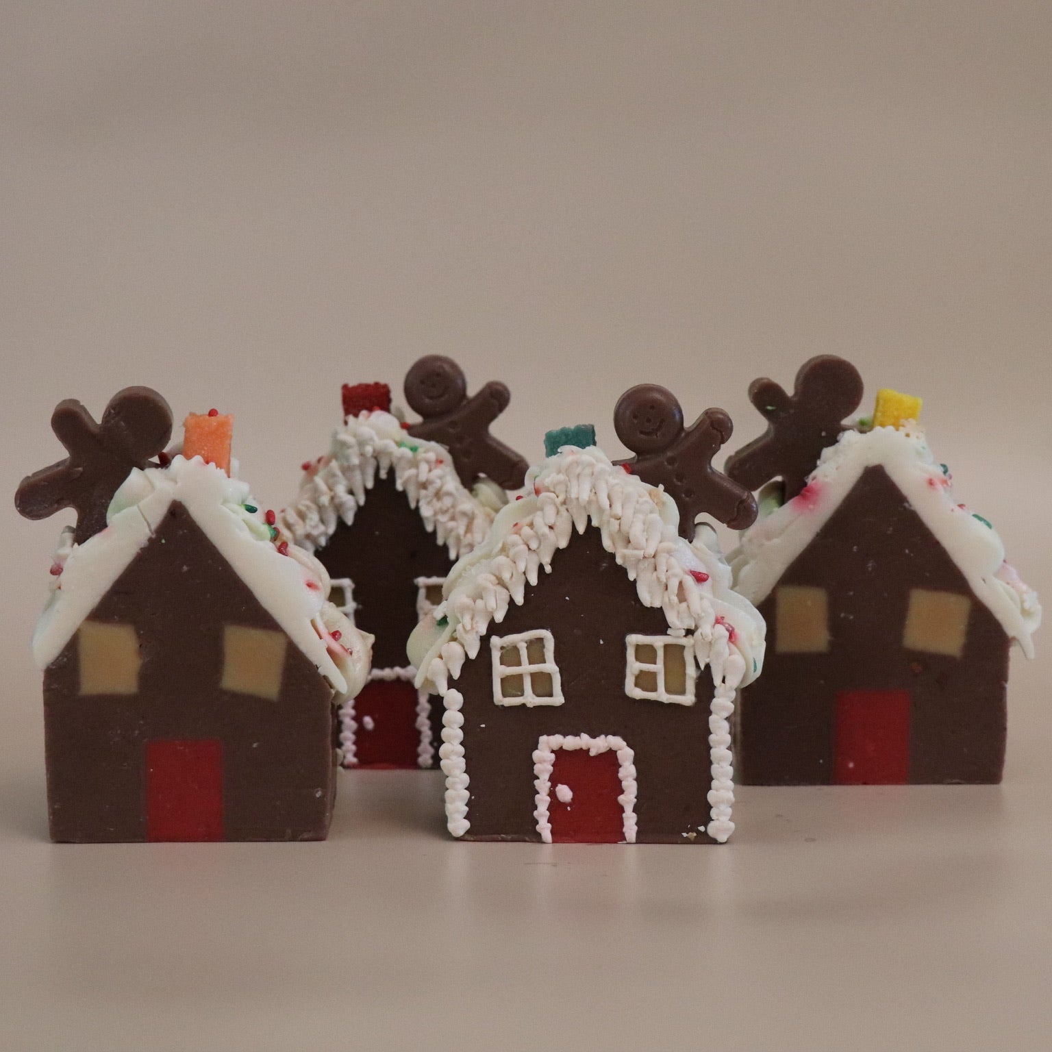 Four gingerbread house artisan soaps with decorative elements on a beige background