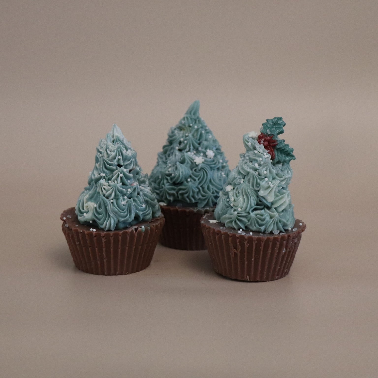 Three chocolate cupcake soaps with dark green frosting shaped like Christmas trees on a beige background