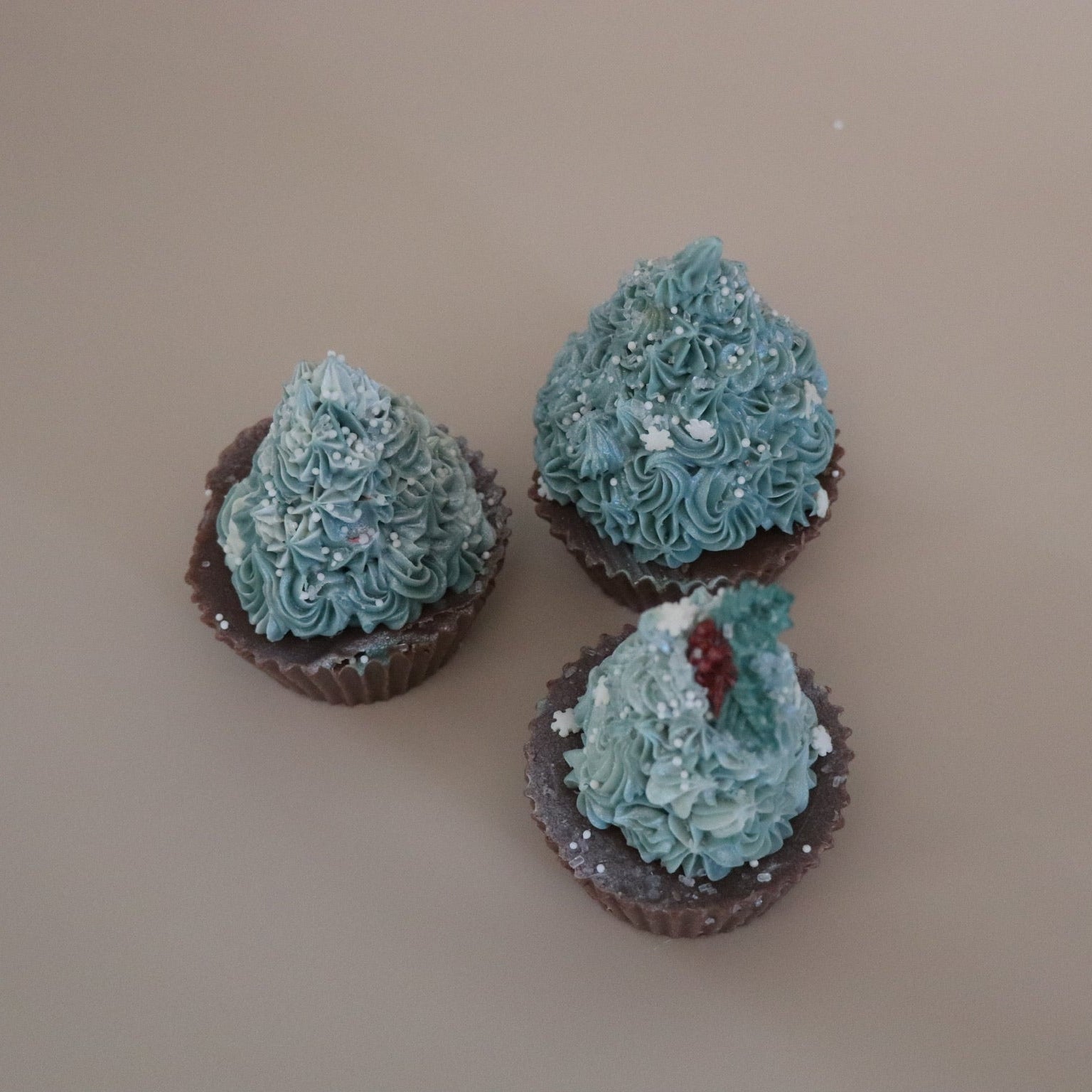 Three small decorative christmas tree cupcake soaps against a beige background