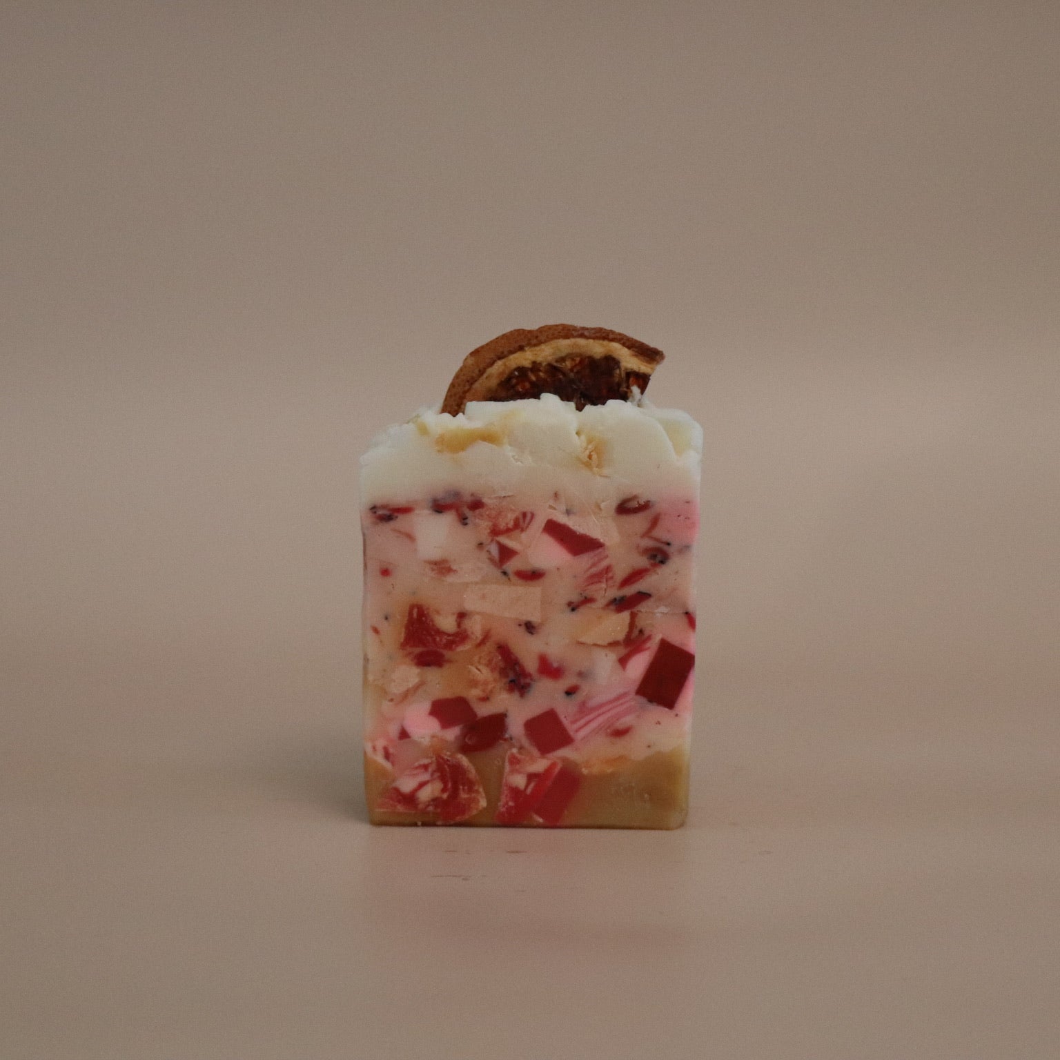 Square soap with white and red speckles and a brown leaf on top against a beige background