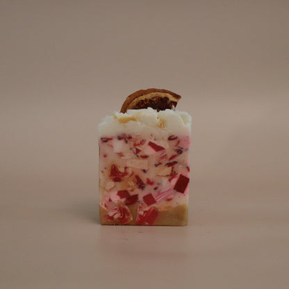 Square soap with white and red speckles and a brown leaf on top against a beige background