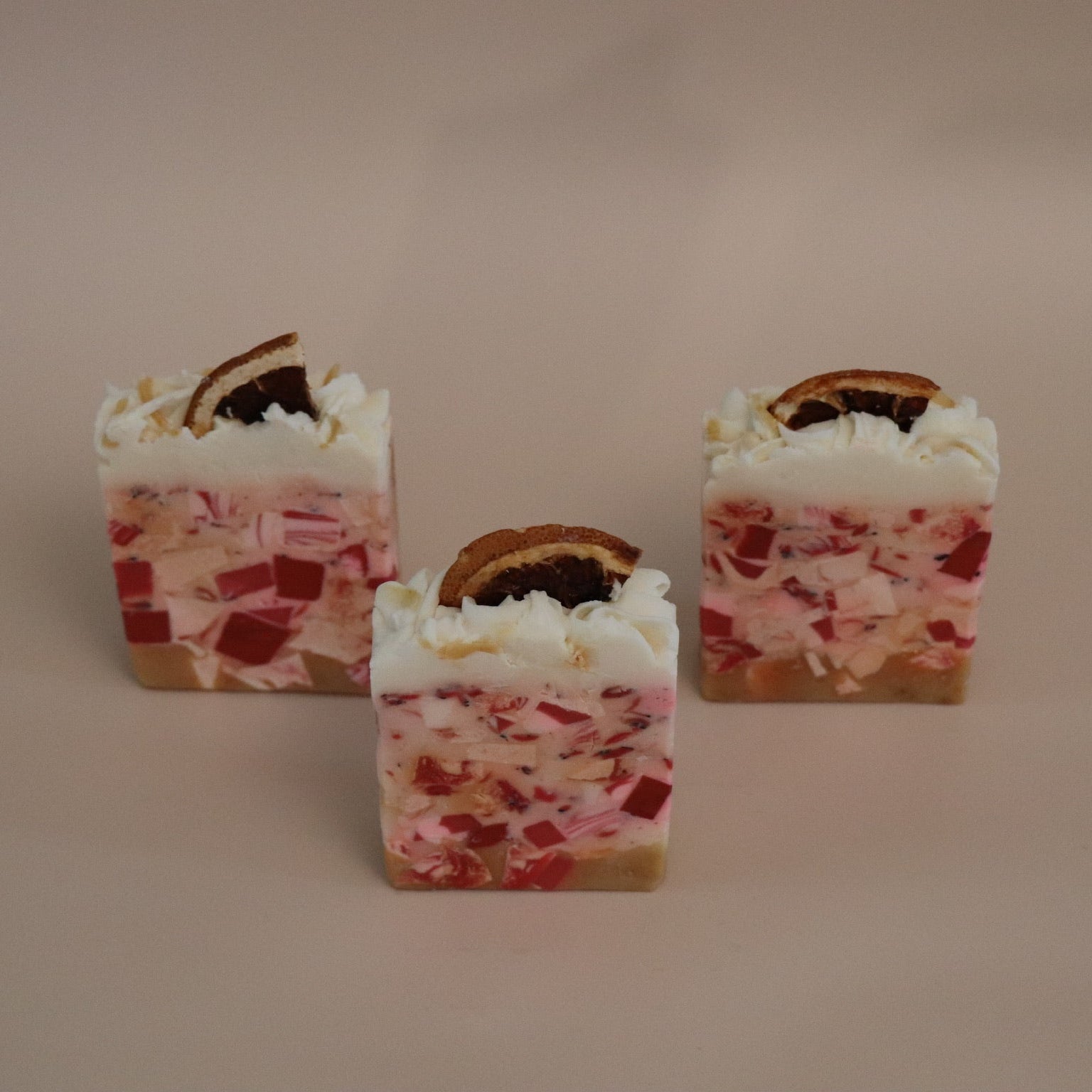 Three small square candies with a red and white pattern on a beige background