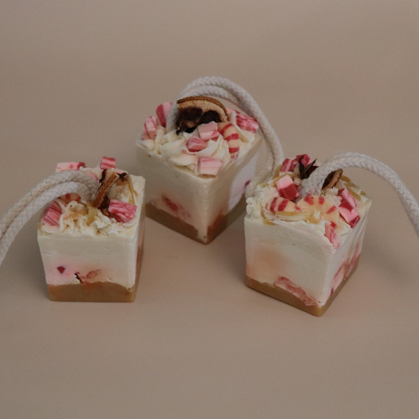Three small square desserts with red and white floral toppings on a beige background