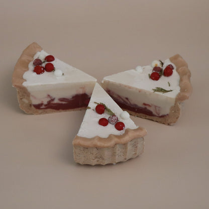 Three slices of Christmas themed pie artisan soaps with white cream and red berries on a beige background