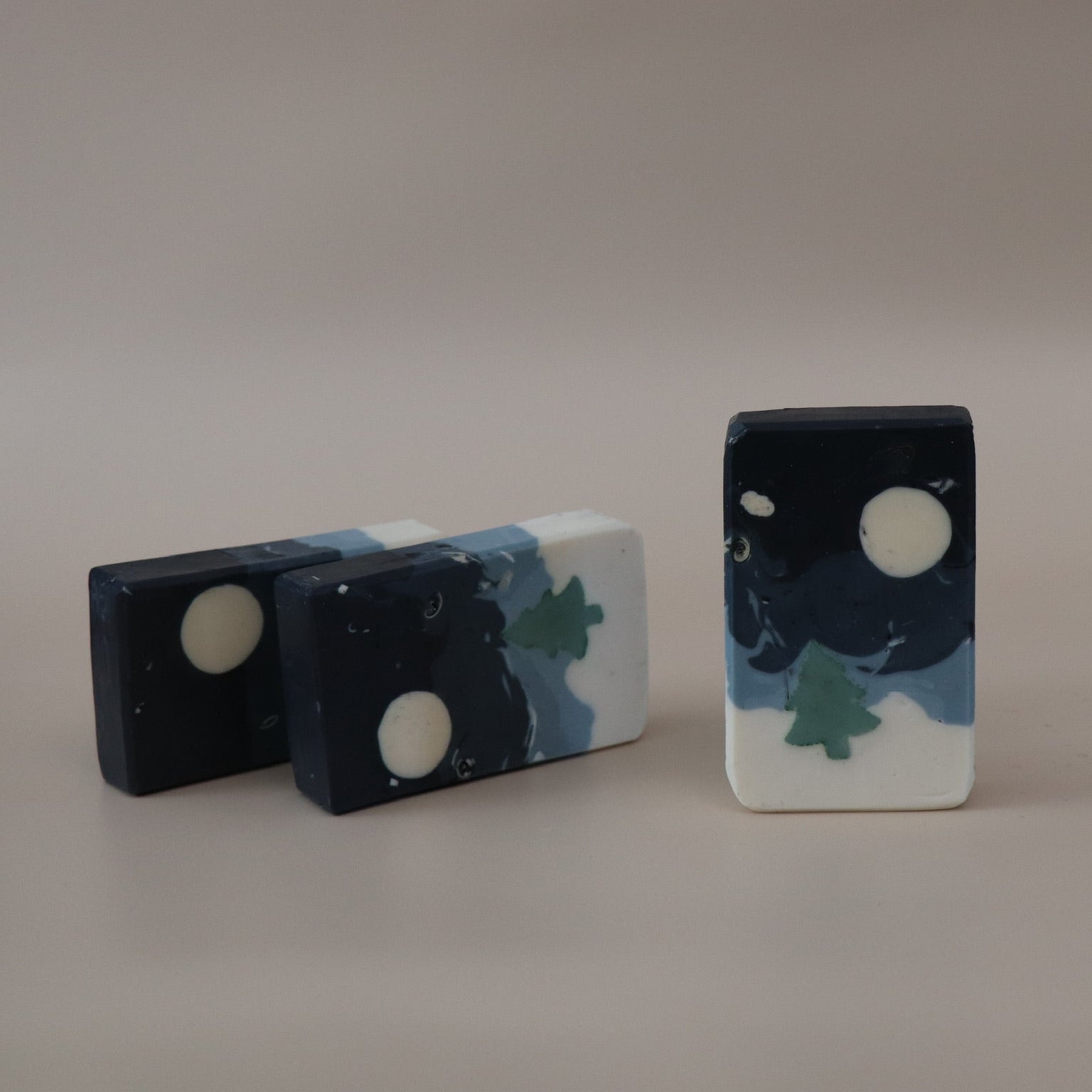 Three decorative stones with night sky and moon designs on a plain background