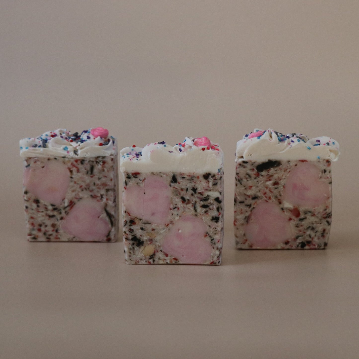 Three square-shaped soaps with floral and pink designs on a beige background