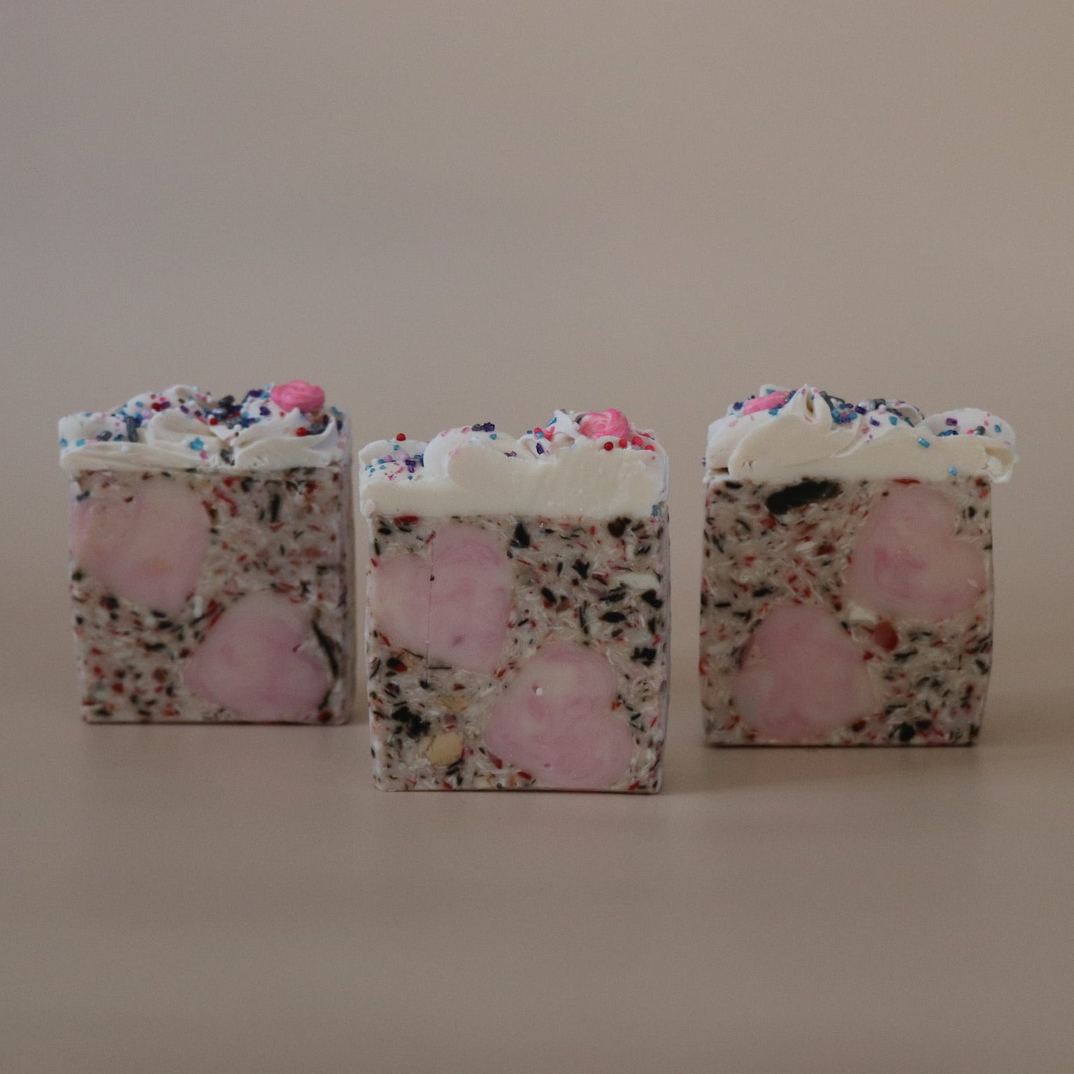 Three square-shaped soaps with floral and pink designs on a beige background