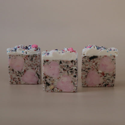 Three square-shaped soaps with floral and pink designs on a beige background
